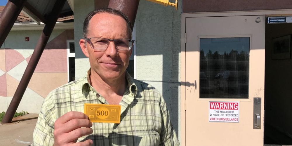 Guidance counselor Kelly Stickle holding the $500 that Charlize gave him outside Mamawi Atosketan Native School in Alberta, Canada. (Andrew McChesney / Adventist Mission)